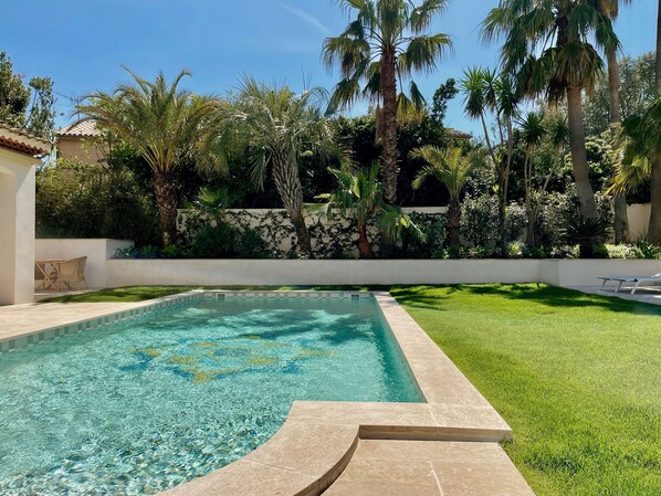 Una piscina con agua cristalina, rodeada de césped cuidado y palmeras.