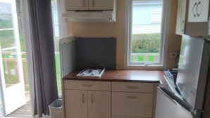 A compact kitchen with a gas stove, a refrigerator, and a window with a view of greenery.