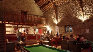 A billiards room with a pool table, wooden beams, stone walls, and a red railing.
