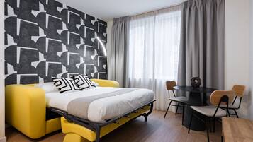 Una habitación moderna con sofá cama tipo futón, una mesa de comedor con sillas y un papel tapiz con motivos geométricos.