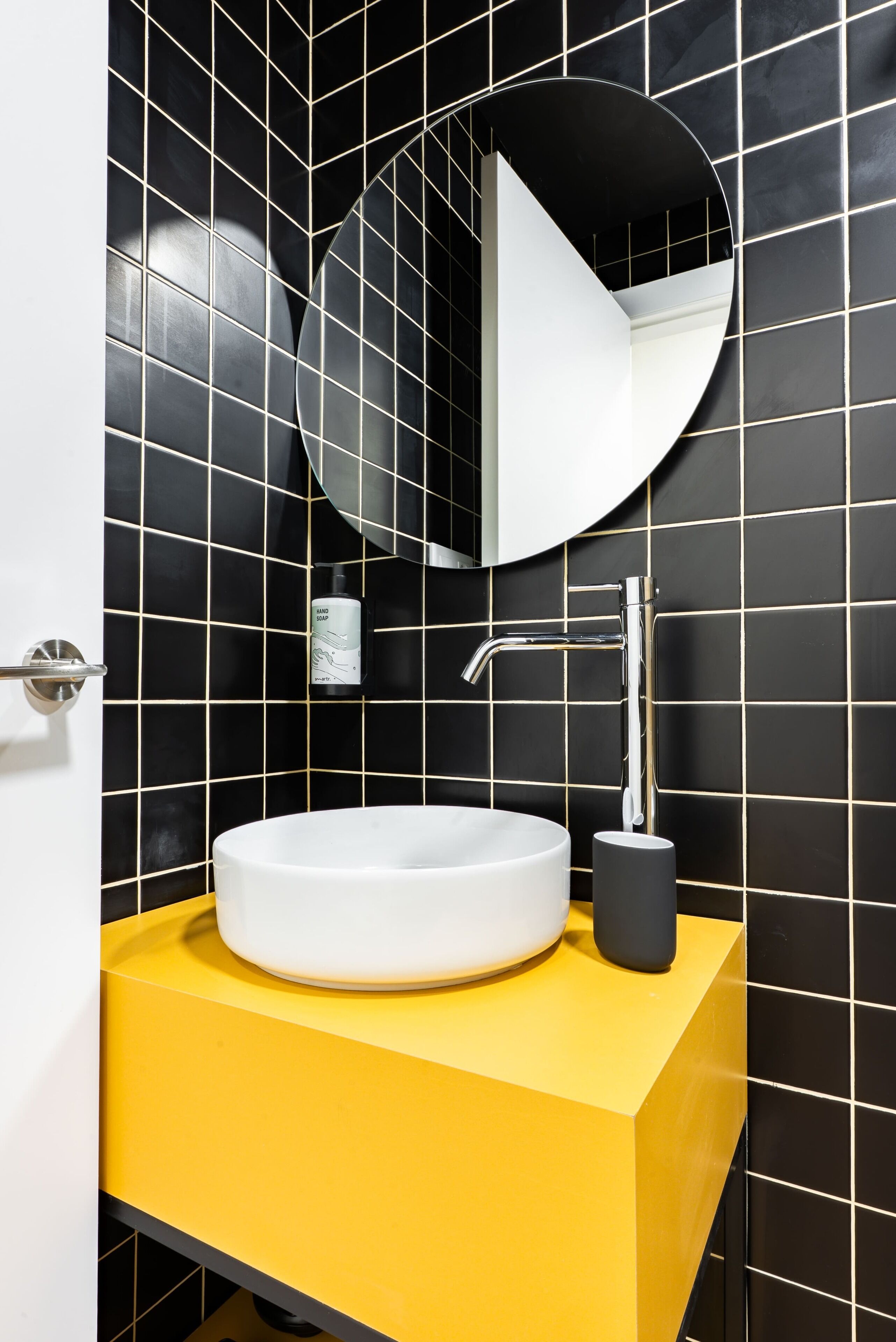 A bathroom with a white sink, a round mirror, and a yellow countertop.