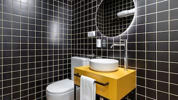A modern bathroom with black tiled walls, a white toilet, a yellow vanity with a white sink, and a mirror above the sink.