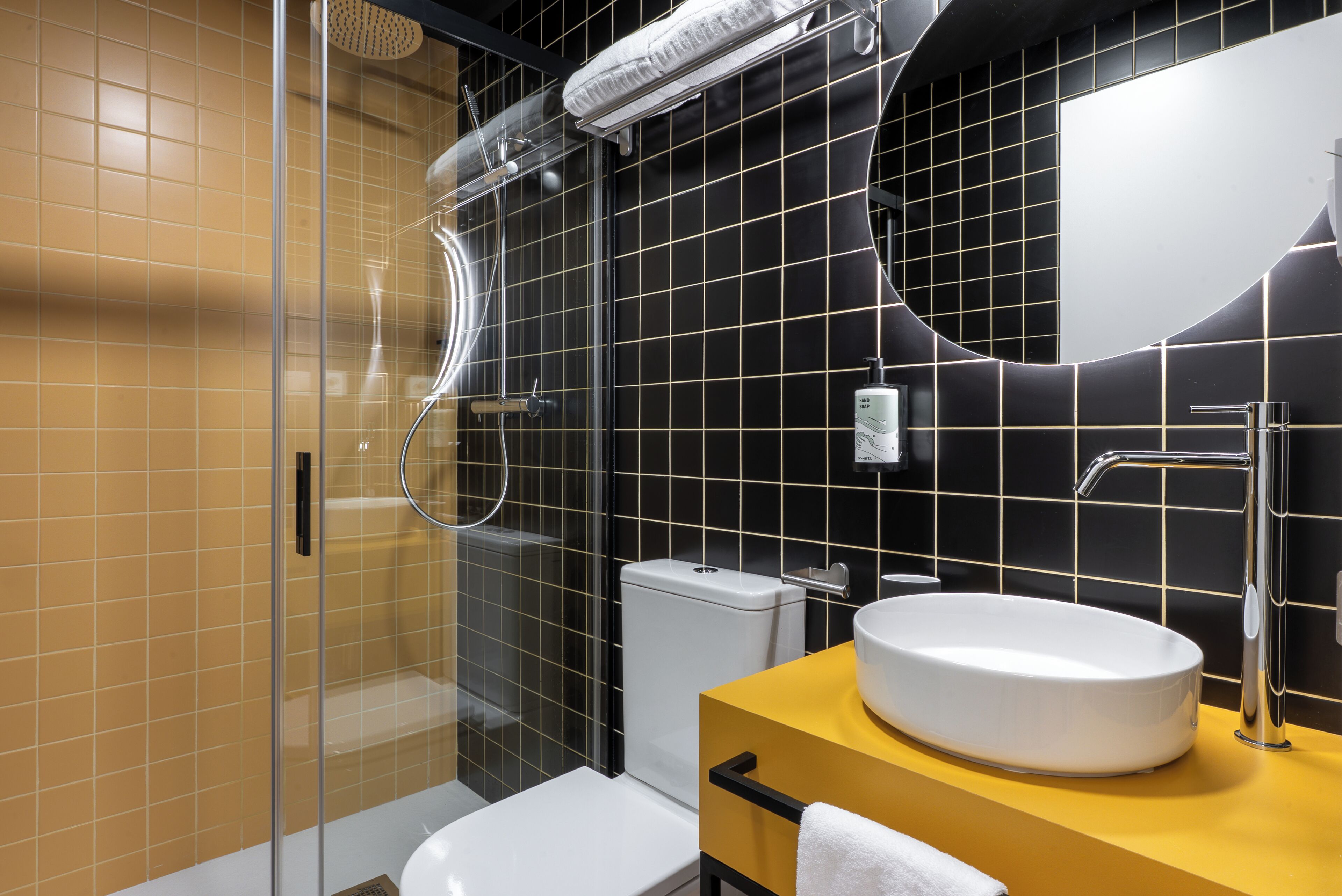 Une salle de bain moderne avec une douche à parois de verre, des toilettes blanches, un lavabo doté d’un plan de toilette jaune et un grand miroir.