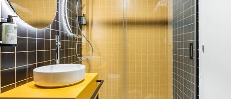 Un baño moderno con un lavabo blanco, un espejo y una zona de ducha.