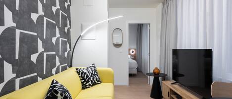 Een moderne woonkamer met een gele bank, een flatscreen televisie en een minimalistisch design.