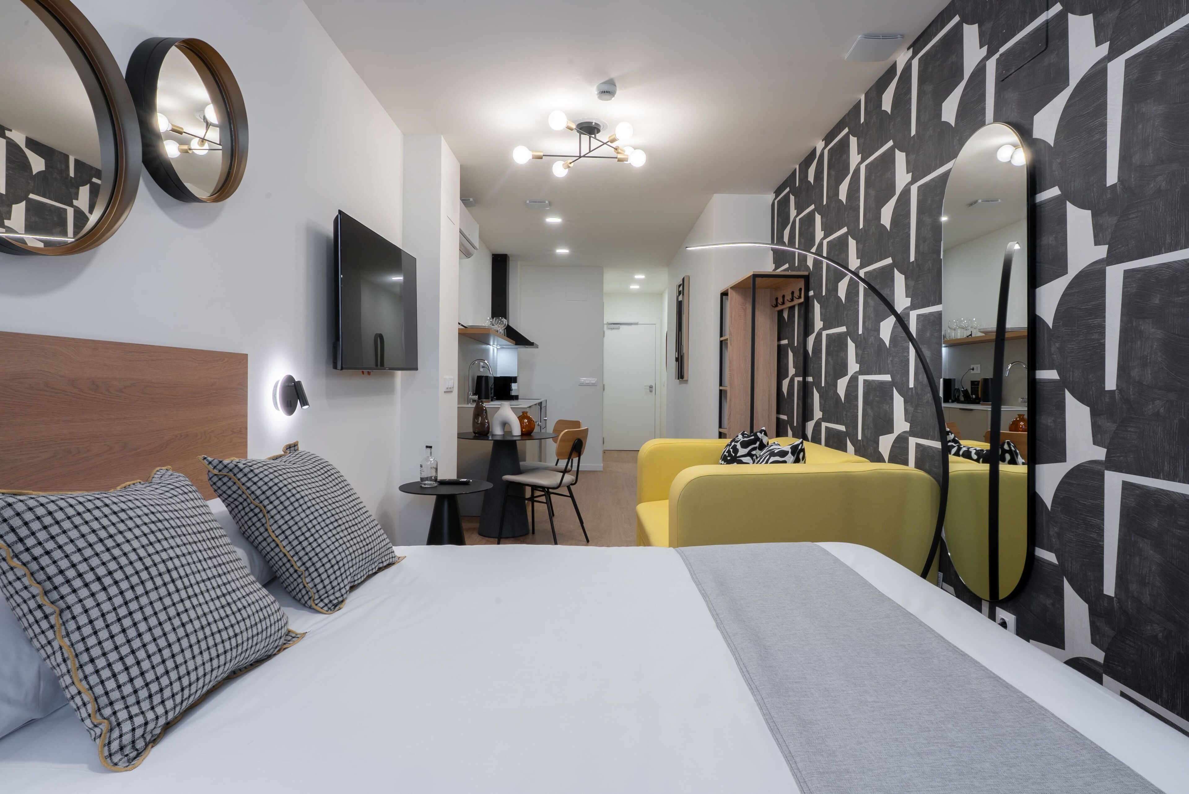 A hotel room with a bed, bedside tables, a TV, a desk, and a yellow sofa.