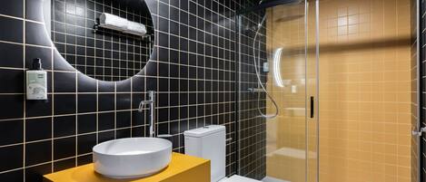 Une salle de bain moderne avec un mur recouvert de carreaux noirs et jaunes, un lavabo blanc et une douche à parois de verre.