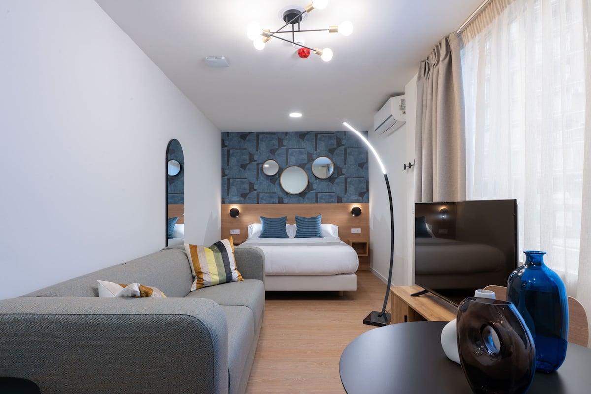 A modern hotel room with a bed, a sofa, a TV, and a desk.