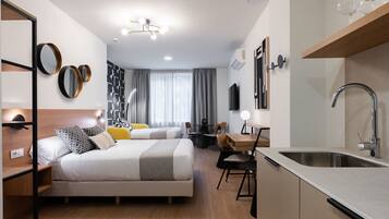 Una habitación de hotel moderna con cama, mesitas de noche, escritorio y una zona de cocina con lavabo.