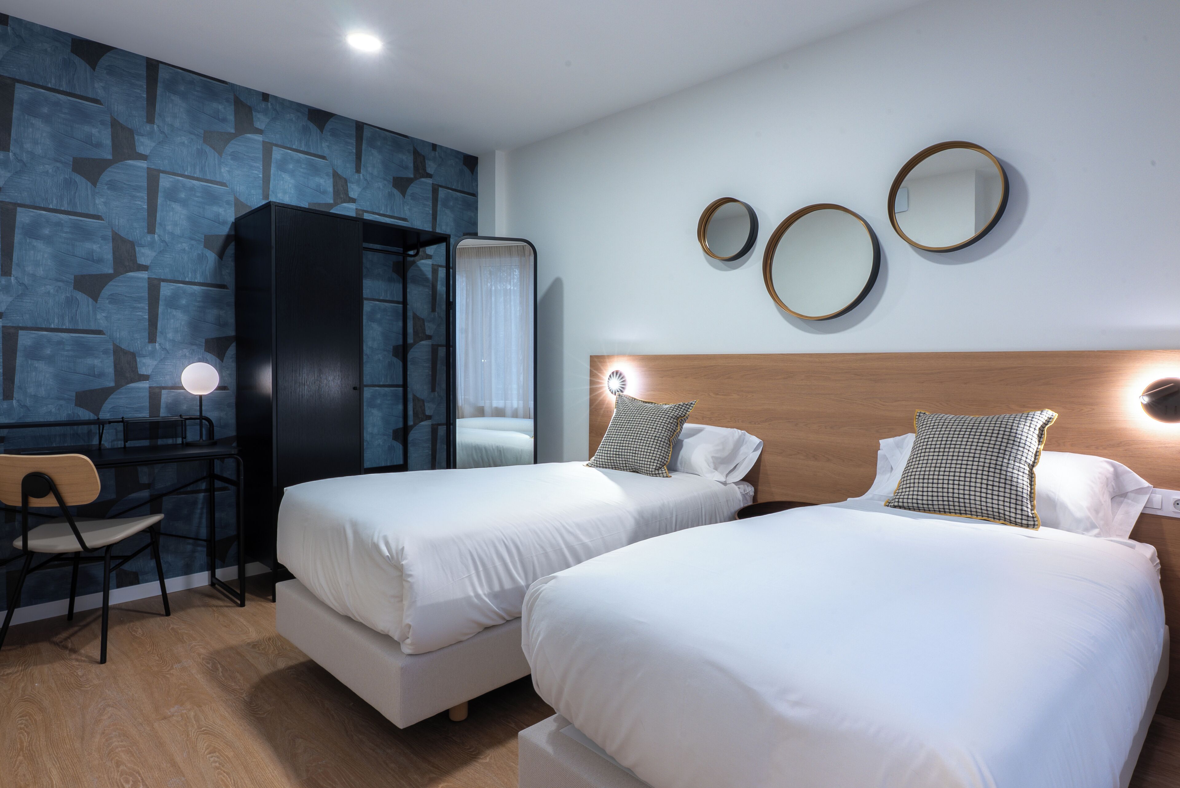 A hotel room with two beds, a desk, a chair, and a wardrobe.