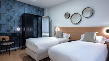 A hotel room with two beds, a desk, a chair, and a wardrobe.