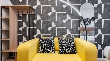 En gul sofa med mønstrede puder, en træreol og en moderne væg med geometriske mønstre.