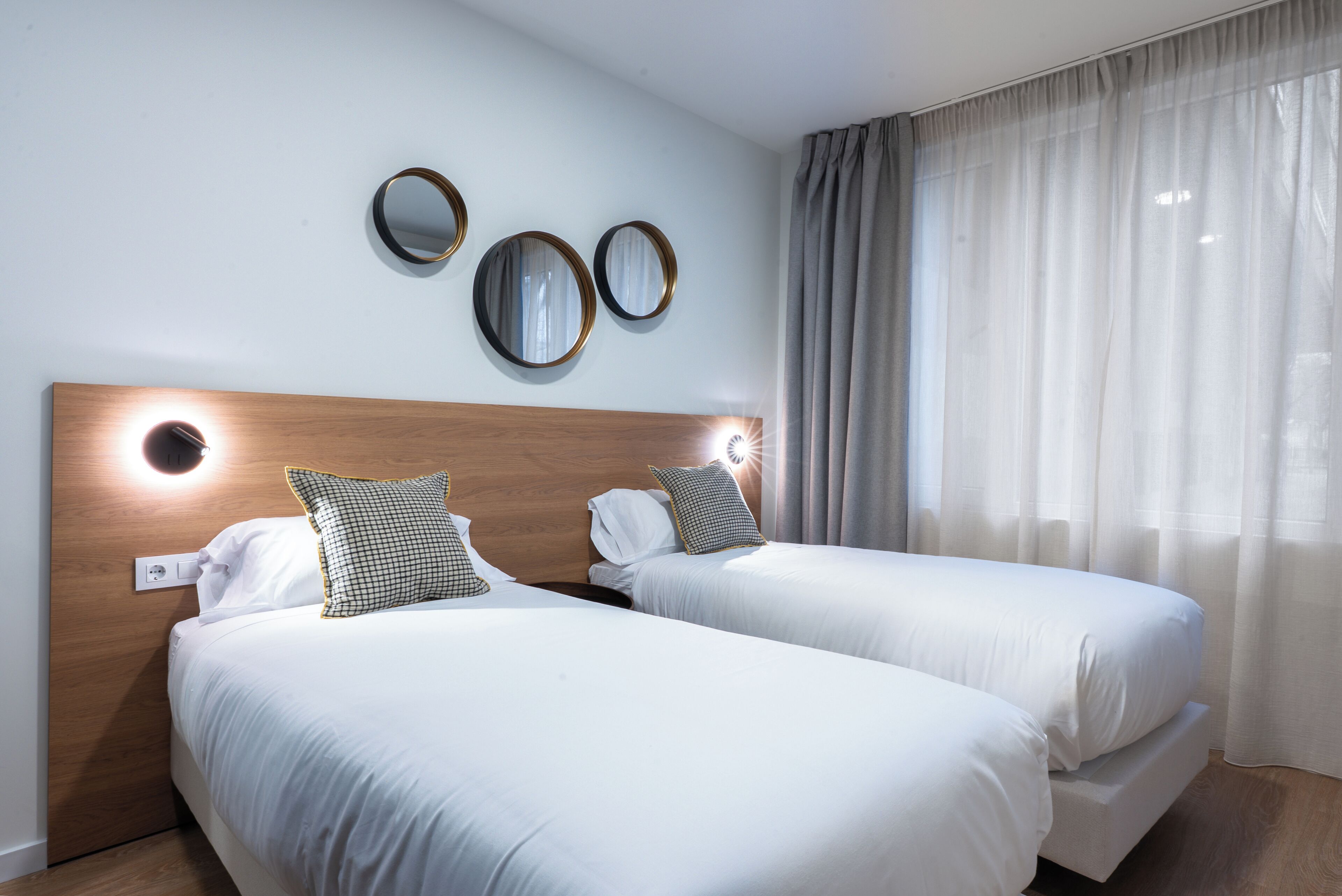 A hotel room with two beds, a wooden headboard, and three wall-mounted mirrors.