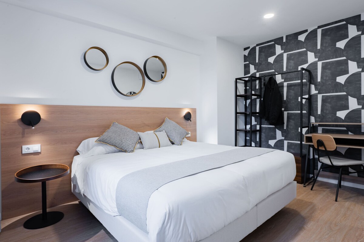 Moderni hotellihuone, jossa on suuri sänky, työpöytä tuolilla sekä naulakko.