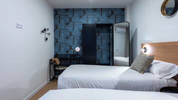 Una habitación de hotel con dos camas, un escritorio, una silla, un espejo y una pared con un diseño geométrico.