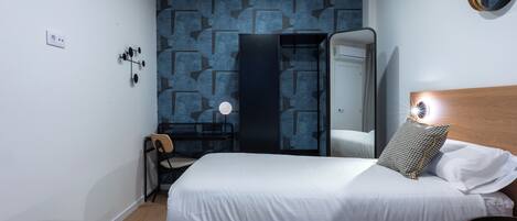 Ein Hotelzimmer mit zwei Betten, einem Schreibtisch, einem Sessel und einem Spiegel, sowie einer Wand mit geometrischem Muster.