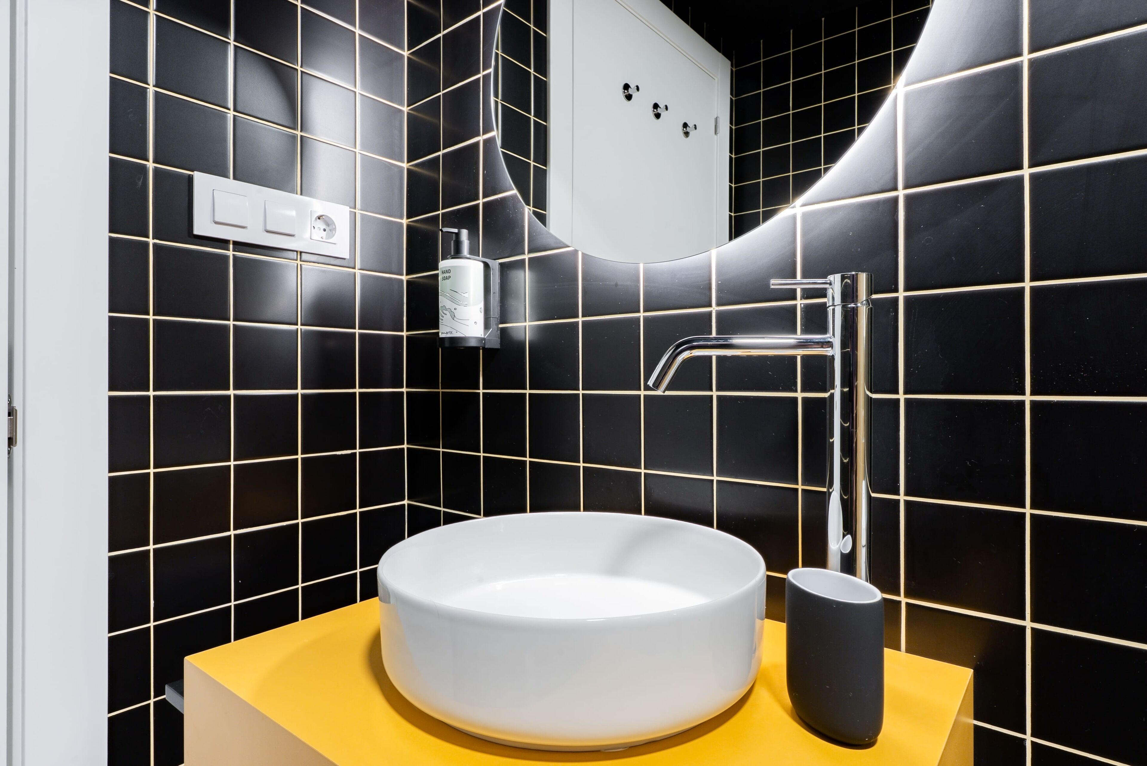 Een badkamer met een wit wastafelblad, een geel aanrecht en zwart betegelde wanden.