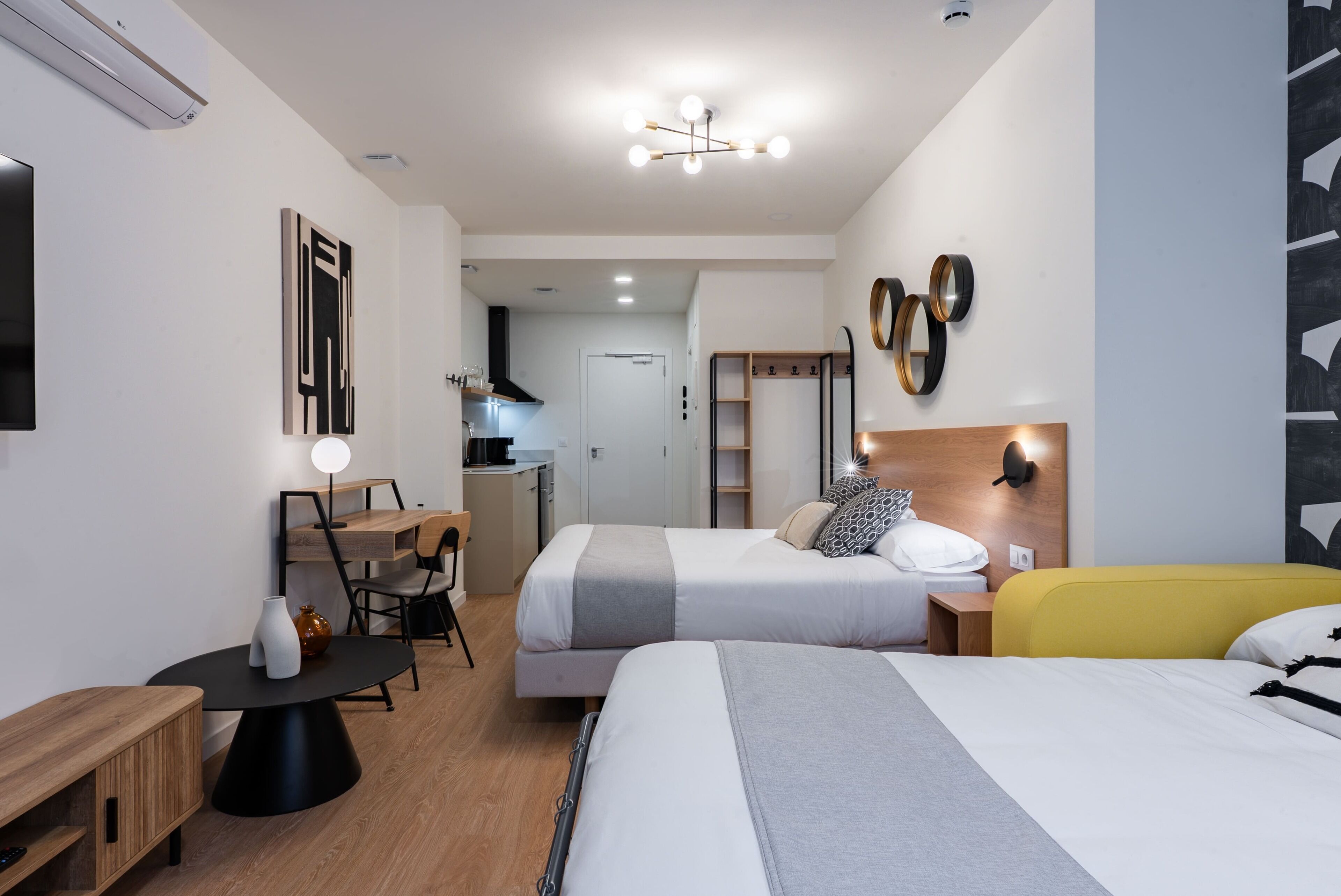 A modern hotel room with two beds, a desk, and a kitchenette.