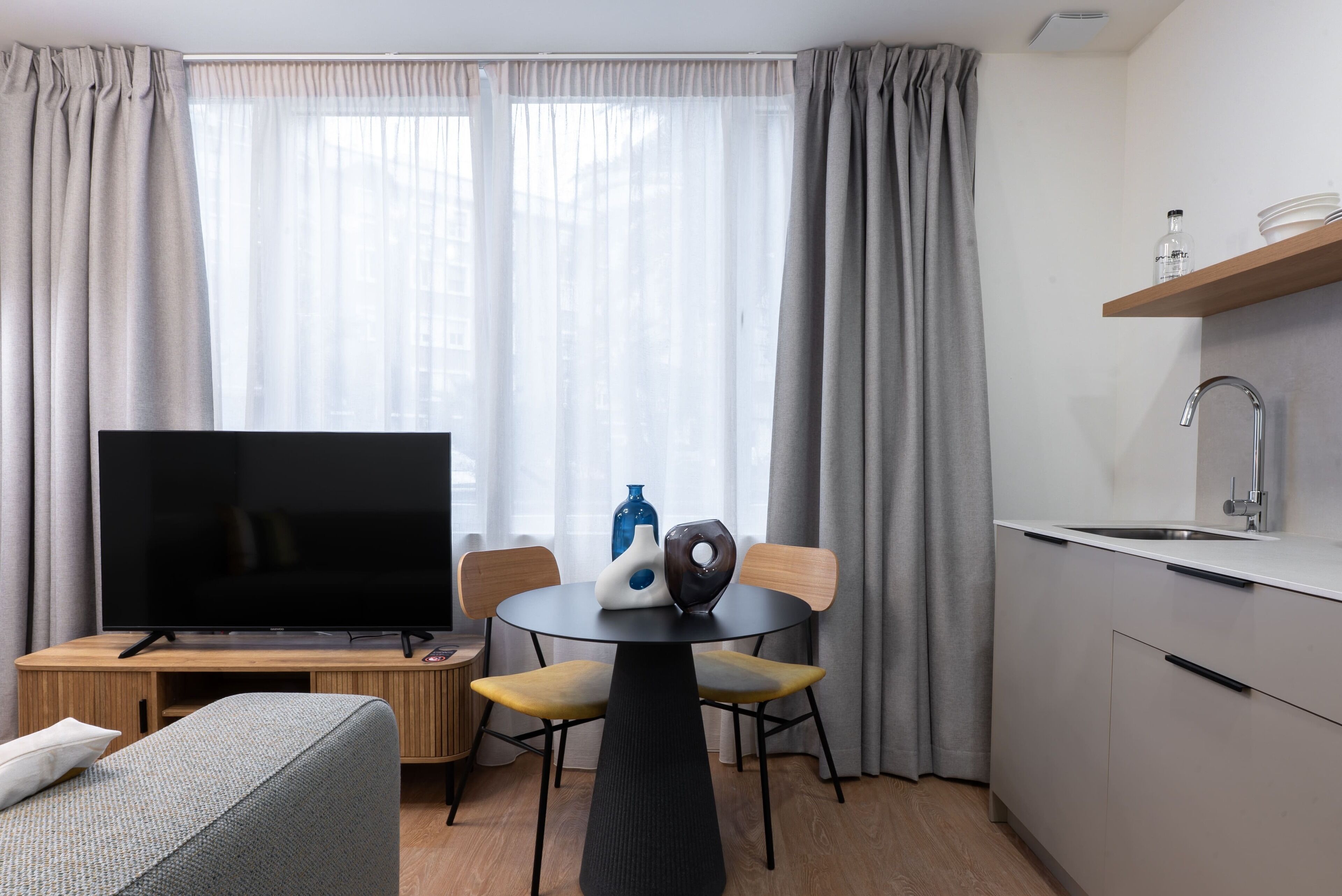 A modern living room with a flat-screen TV, a round dining table, and a sofa.