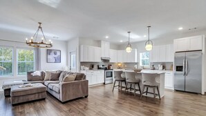 A modern kitchen with white cabinets, a stainless steel refrigerator, and a dining area with bar stools.