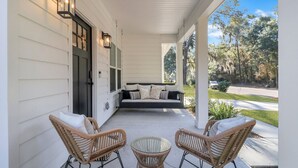 A covered porch with wicker chairs, a glass table, and a black sofa with cushions.