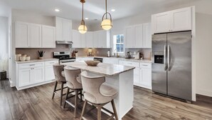 A modern kitchen with white cabinetry, a central island with bar stools, stainless steel appliances, and pendant lighting.