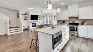 A modern kitchen with white cabinetry, a central island, stainless steel appliances, and pendant lighting.