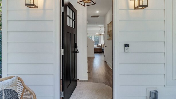 A hallway with a black door, white walls, and two wall-mounted lanterns.