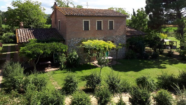 A rustic brick house with a tiled roof, surrounded by a well-maintained garden and trees. - Appartamento Scuderia Del Borgo (Monteleone d'Orvieto)
