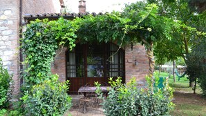 A brick building with a covered patio, a table and chairs, and a garden area. - Appartamento Scuderia Del Borgo (Monteleone d'Orvieto)