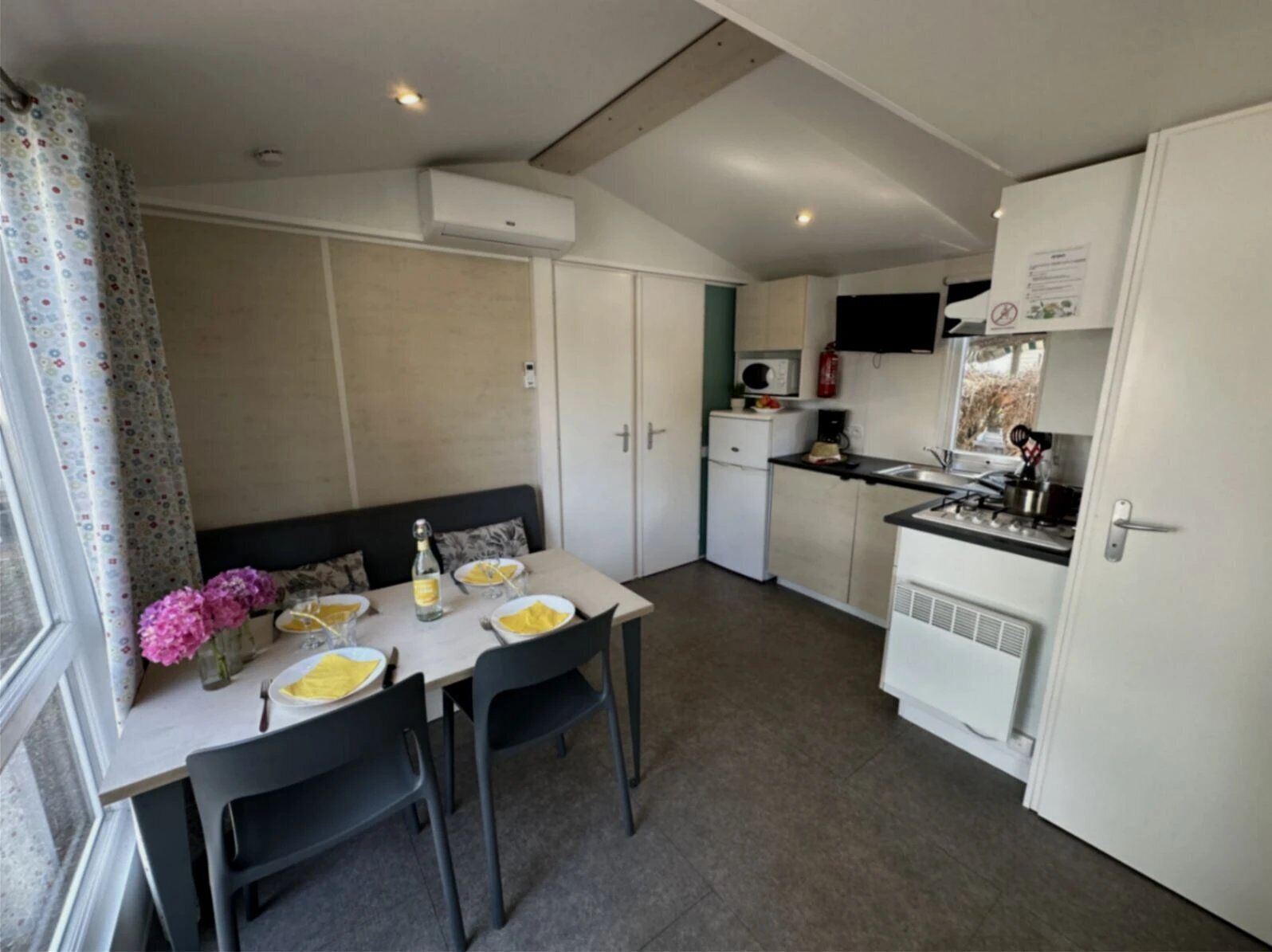 Cocina compacta con comedor, que incluye una mesa para dos personas, un microondas y un refrigerador pequeño.