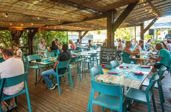 Un área de comedor al aire libre con mesas y sillas de madera, un menú en una pizarra y vistas al mar.