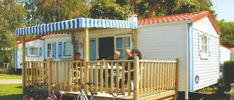 A mobile home with a porch and a covered area, bicycles parked in front, and a clear sky in the background.