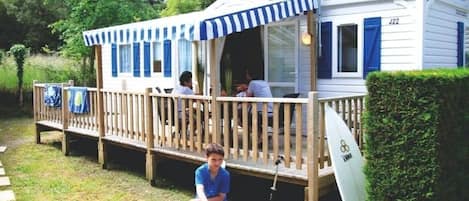 A mobile home with a deck, a surfboard, and a bicycle.