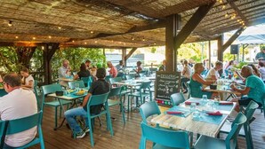 Un espace de restauration en plein air avec des tables et des chaises en bois, un menu écrit à la craie et une vue sur la mer.