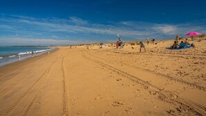 Une vaste plage de sable où l’on peut voir des empreintes de pas et quelques personnes.
