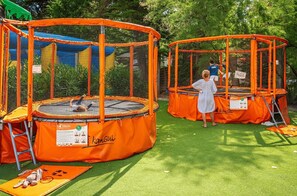 Two outdoor trampolines with safety nets, surrounded by trees.