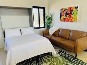 Relax in this serene bedroom with a large bed, a comfortable sofa, and a vibrant art piece.
