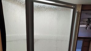 Ett kök med en dörr av frostat glas, träskåp och en bänkskiva av granit.