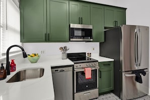 Une cuisine avec des meubles de couleur verte, un réfrigérateur en acier inoxydable, un four à micro-ondes, une cuisinière et un lave-vaisselle.
