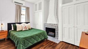 A bedroom with a green bed, a fireplace, white doors, and a ceiling fan.