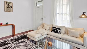 A living room with a sofa, a glass coffee table, a patterned rug, a wooden console table with decorative items, and a door with a window.