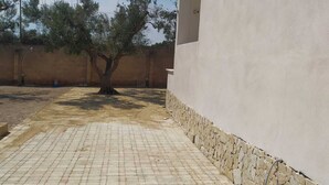 Un patio empedrado con un árbol, una pared blanca y una pared de piedra.