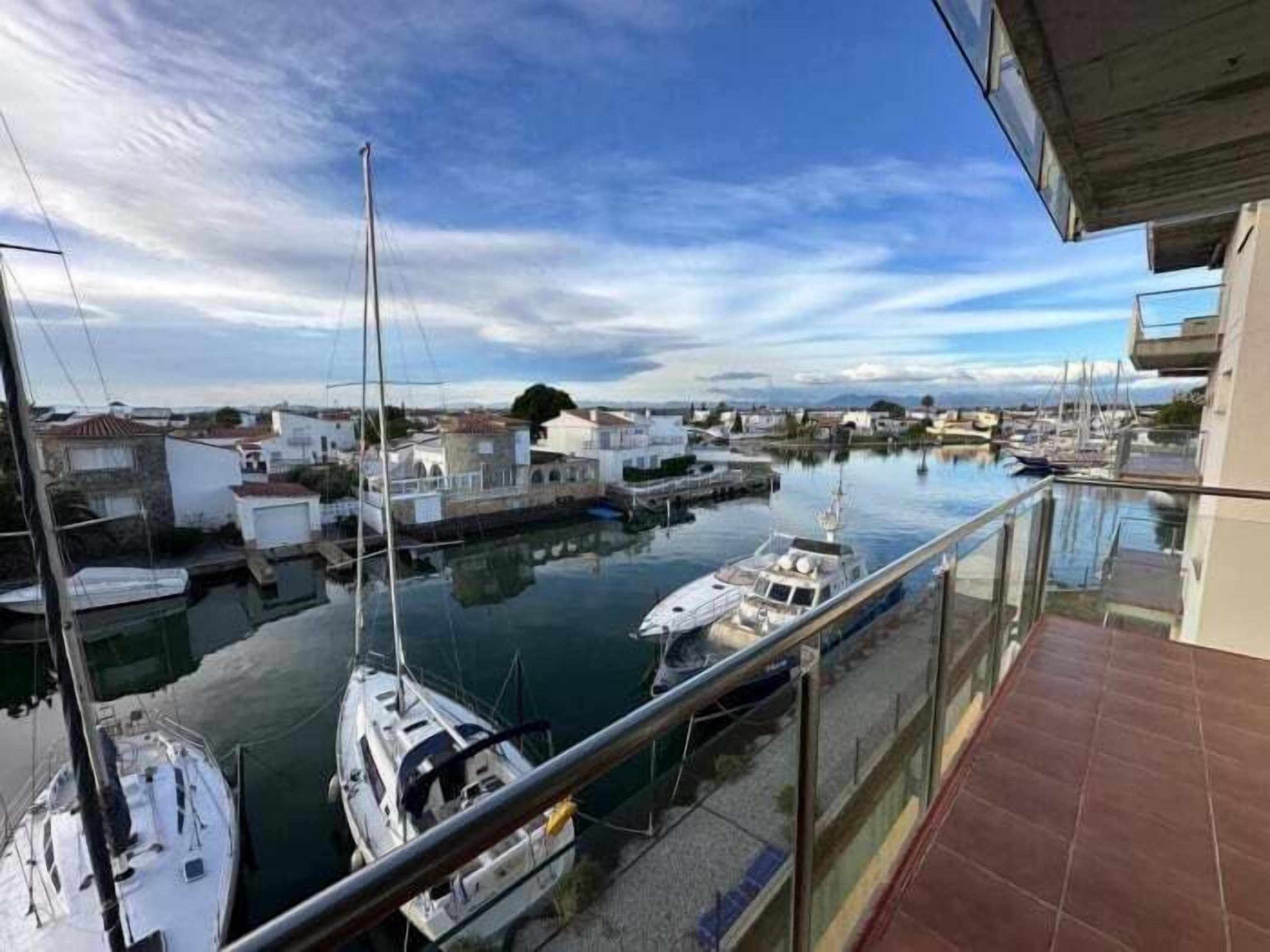 A marina with boats docked, a clear sky, and buildings in the background.