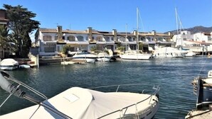 A marina with boats docked, buildings with Mediterranean architecture, and a clear blue sky. - Flat in Roses with canal view and swimming pool AV 52 (Roses)