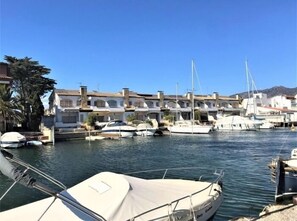 A marina with boats docked, buildings with Mediterranean architecture, and a clear blue sky.