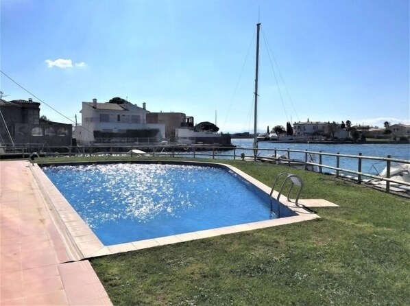 A swimming pool with a grassy area and a view of a marina and buildings in the background. - Flat in Roses with canal view and swimming pool AV 52 (Roses)