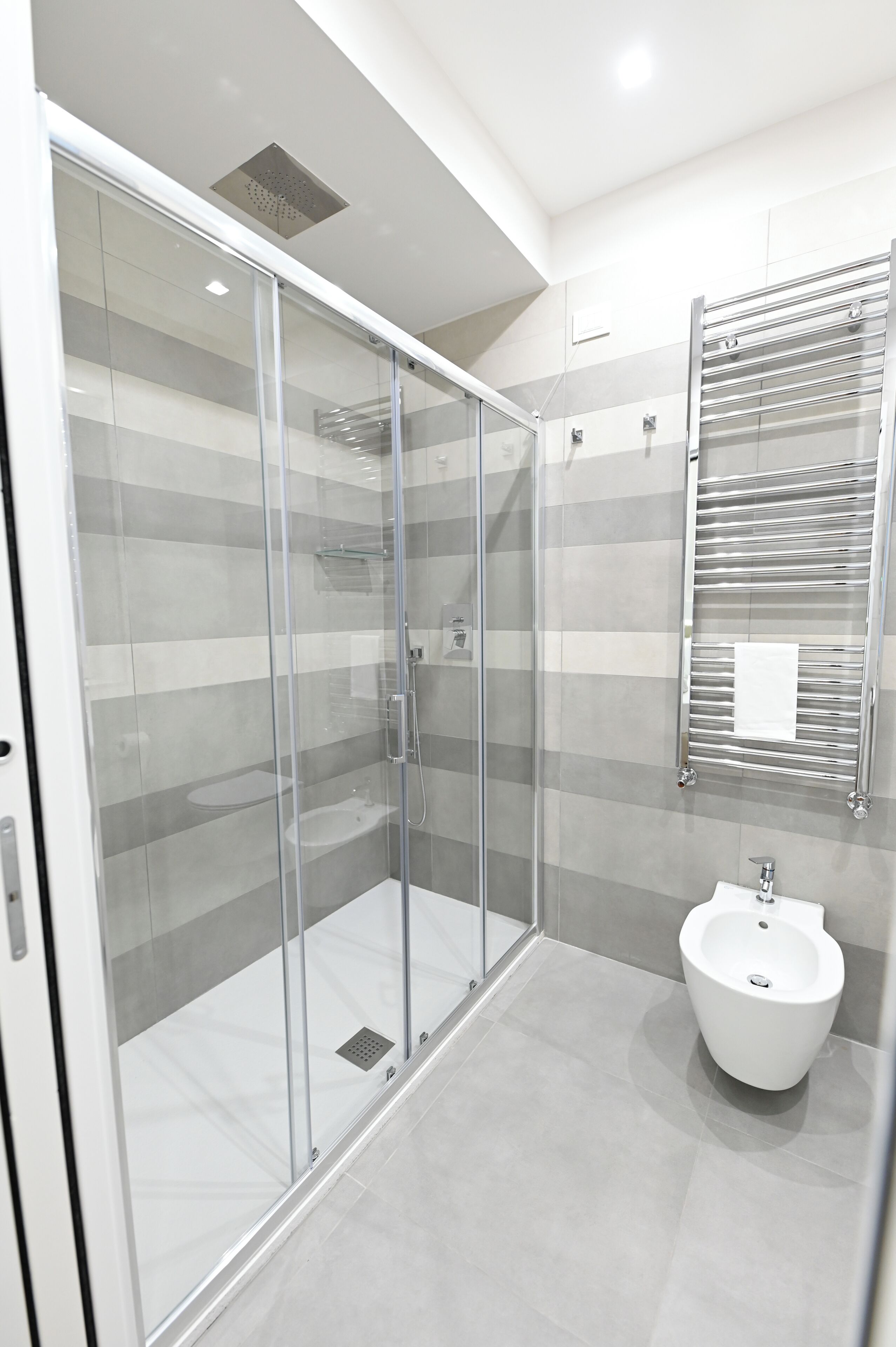 A modern bathroom with a glass-enclosed shower, a white pedestal sink, and a towel rack.
