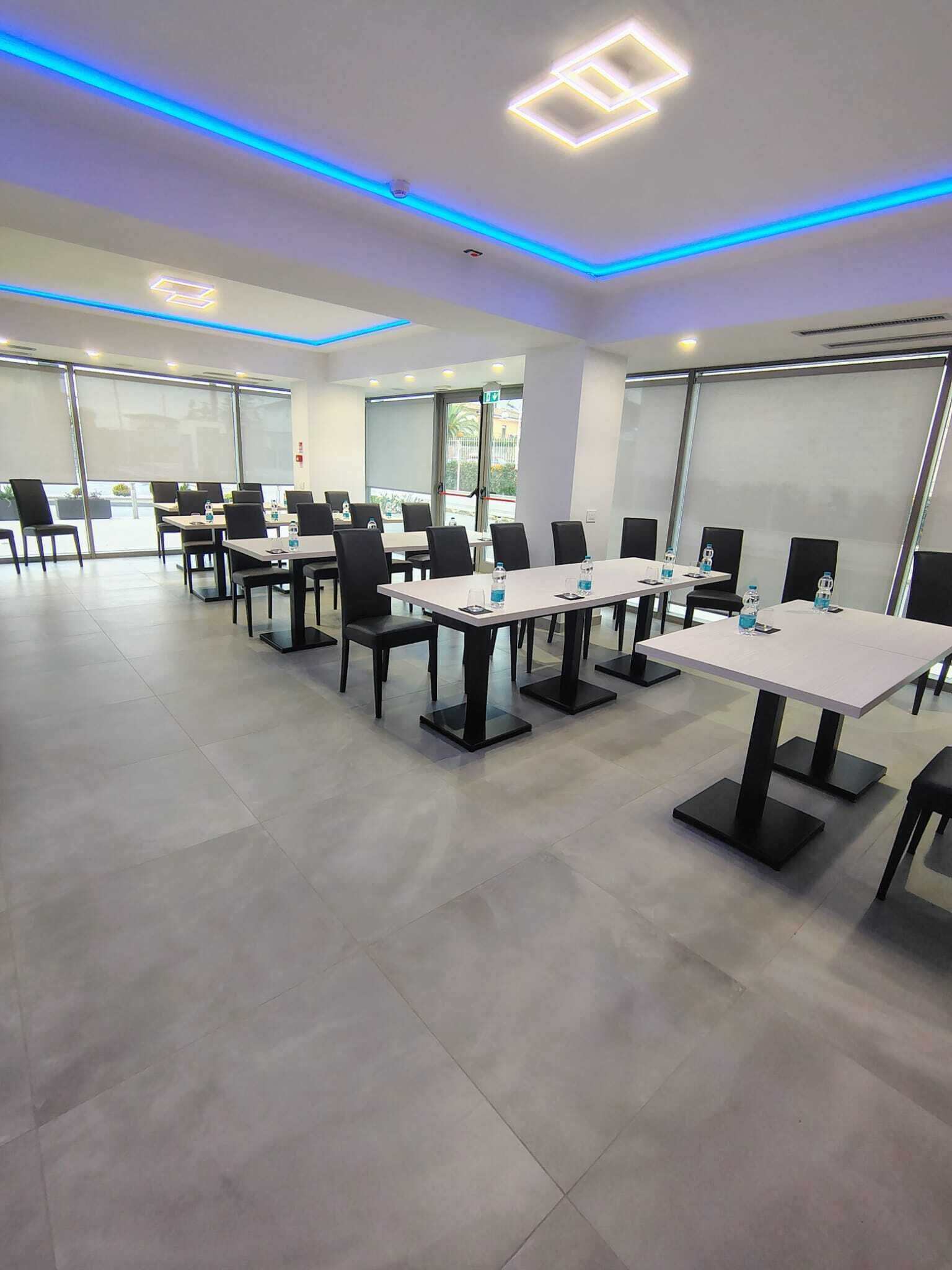 Un salón de conferencias con mesas y sillas, ventanas amplias e iluminación LED azul en el techo.
