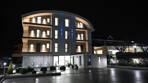 Ein modernes Hotel mit geschwungener Fassade, mehreren Balkonen und einem gut beleuchteten Eingangsbereich mit Pflanzgefäßen.
